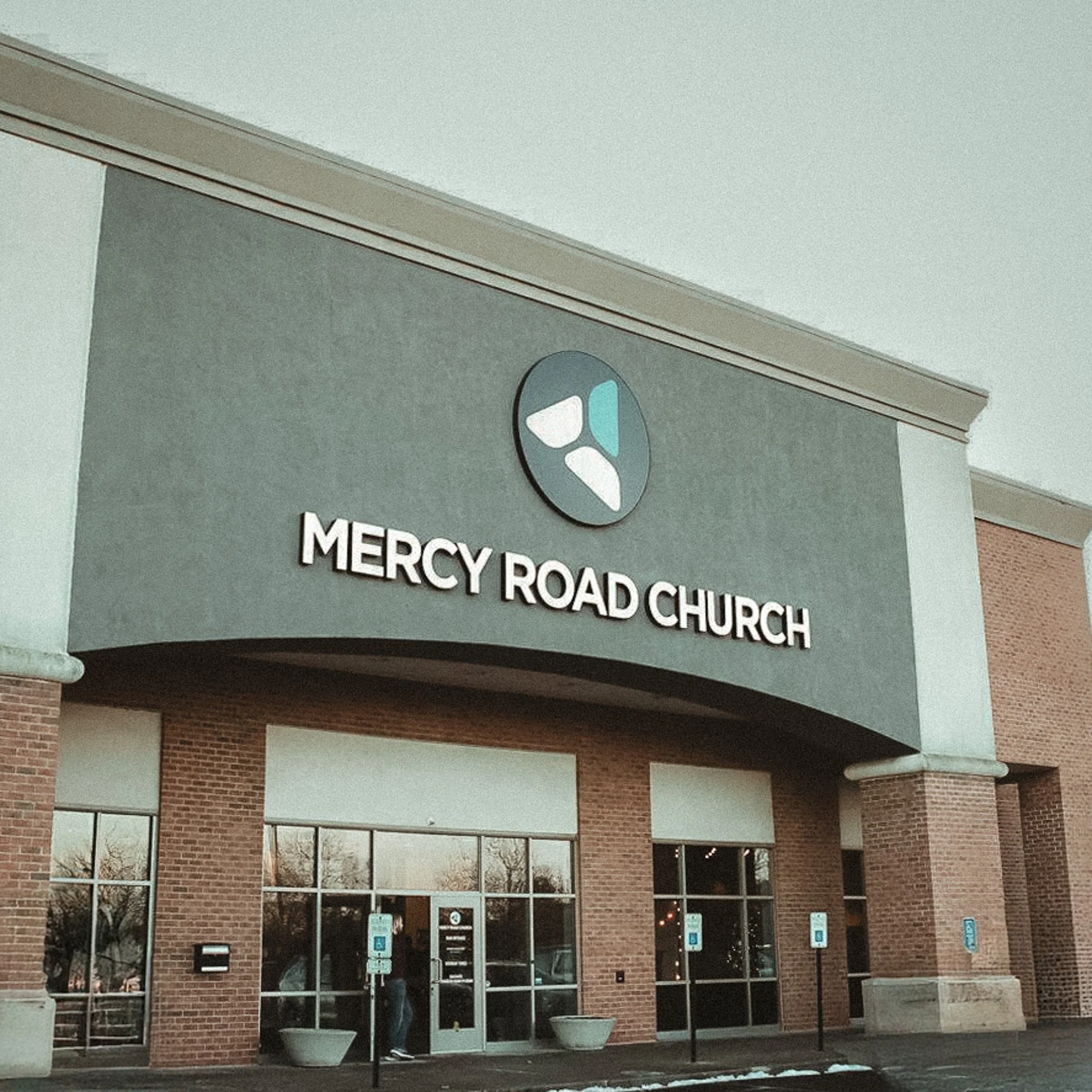 Exterior entrance of Mercy Road Church with logo above the doorway and brick walls.